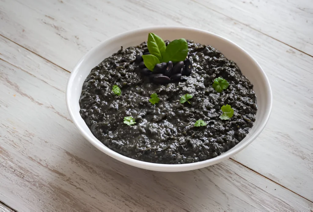 A bowl of flavorful chipotle black beans garnished with fresh cilantro and lime, served with tortillas and a side of rice.