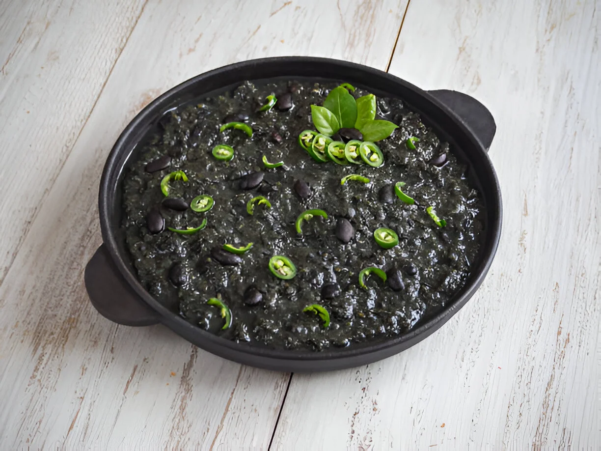 A bowl of flavorful chipotle black beans garnished with fresh cilantro and lime, served with tortillas and a side of rice.