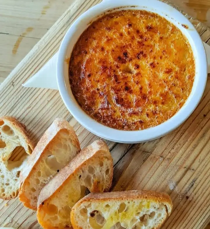 Image of individual servings of crab brulee in ramekins, showcasing the golden-brown caramelized sugar topping and a hint of crab meat peeking through.