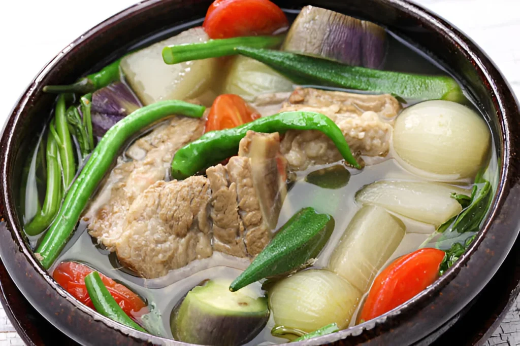 A bowl of steaming Sinigang soup made with pork, fresh vegetables, and tamarind.