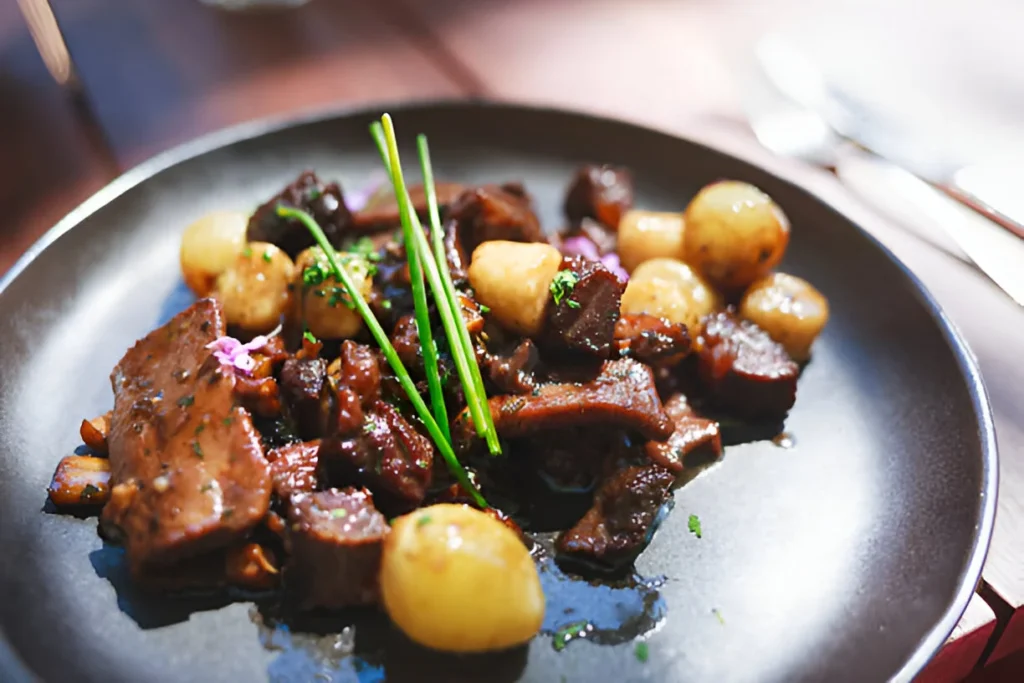 A beautifully roasted venison roast garnished with fresh herbs, served alongside mashed potatoes and roasted vegetables on a rustic wooden table.