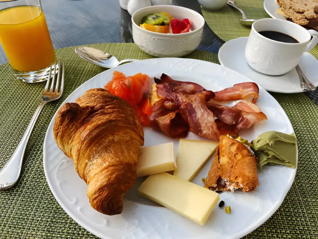 A plate of freshly baked gipfeli pastries, showcasing their flaky layers and golden-brown color, alongside a cup of coffee and fruit preserves.