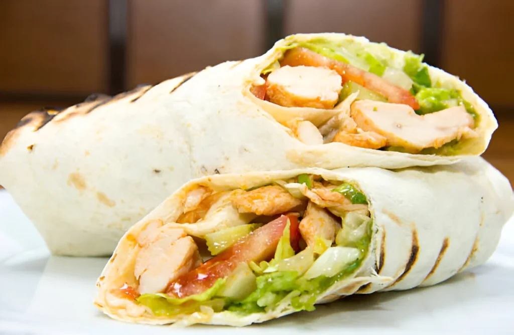 Grilled chicken wrap filled with fresh vegetables and served on a plate.