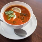 A bowl of homemade tomato soup garnished with fresh basil and served with crusty bread.