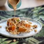 A slice of pumpkin dump cake topped with whipped cream and a drizzle of caramel sauce, served on a rustic wooden table.