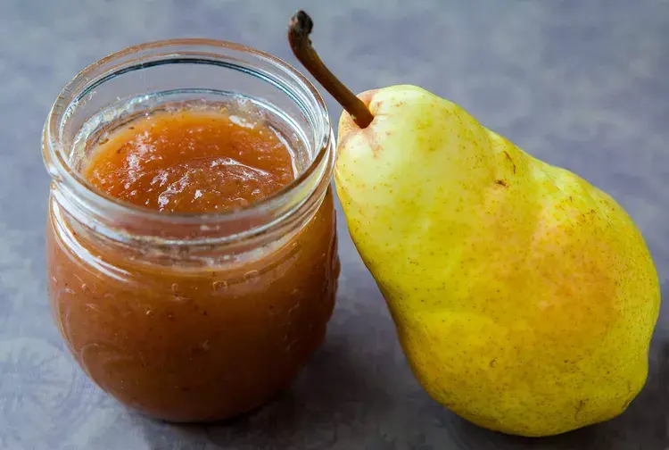 A jar of homemade pear butter with a slice of toast and fresh pears.