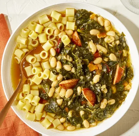 A bowl of vibrant swamp soup garnished with fresh herbs and accompanied by crusty bread.